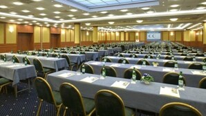Une grande salle de conférence avec de nombreuses rangées de tables et de chaises, équipée de plaques nominatives et de bouteilles d’eau.