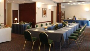 Une salle de conférence avec de longues tables, des chaises vertes et une nappe bleue.
