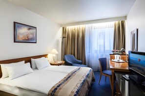 A hotel room with a large bed, a desk with a computer, a chair, a TV, and a painting on the wall. - Danubius Hungaria City Centre (Budapest)