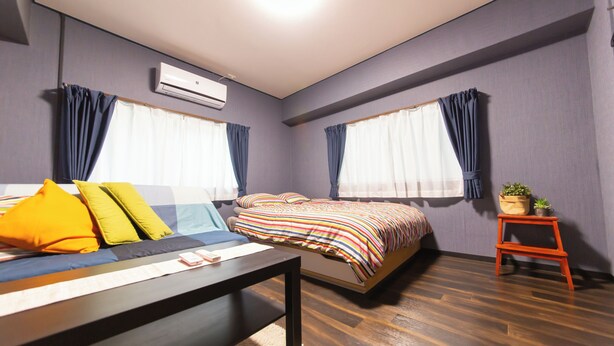 A modern bedroom with a bed, a bedside table, a small table with a plant, and a window with curtains. - Cozy Modern Apartment | Walk to Tanimachi & Easy Access to Namba & Osaka Castle (Osaka-cty,Tennoujiku,Shimizudani-chou)