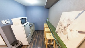 A compact kitchen with a microwave, stove, and small trash bin. There are wooden stools and a painting on the wall. - Cozy Modern Apartment | Walk to Tanimachi & Easy Access to Namba & Osaka Castle (Osaka-cty,Tennoujiku,Shimizudani-chou)