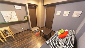 A compact room with a wooden floor, a sofa with a patterned cover, a small table, and a chair. - Cozy Modern Apartment | Walk to Tanimachi & Easy Access to Namba & Osaka Castle (Osaka-cty,Tennoujiku,Shimizudani-chou)