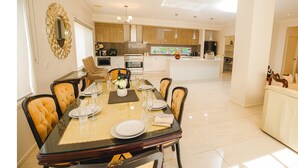 Une cuisine moderne dotée d’un îlot central, un coin repas avec une table en verre et un salon avec un canapé et des fauteuils.