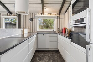 Una cocina con armarios blancos, encimera negra, ventana y horno empotrado.