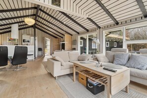 A spacious living area with a high ceiling, a sofa set, a coffee table, and a view through large windows.