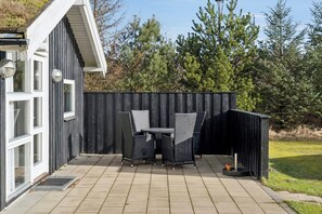 A patio with a table and chairs, a small shed, and a wooden fence. - Lovely holiday home with spa, sauna and peace (Fjerritslev)