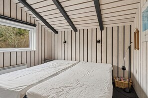 A room with two beds, a window, a wall-mounted lamp, and a wicker basket. - Lovely holiday home with spa, sauna and peace (Fjerritslev)