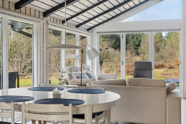 A modern, open-plan living space with a dining area, seating, and large windows offering a view of the outdoors.