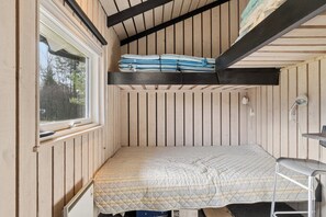 Una habitación pequeña con literas, un escritorio reducido y una ventana.