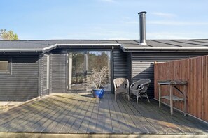 A deck with a potted plant, two wicker chairs, and a wooden fence. - Renovated holiday home near beach and town (Blokhus)