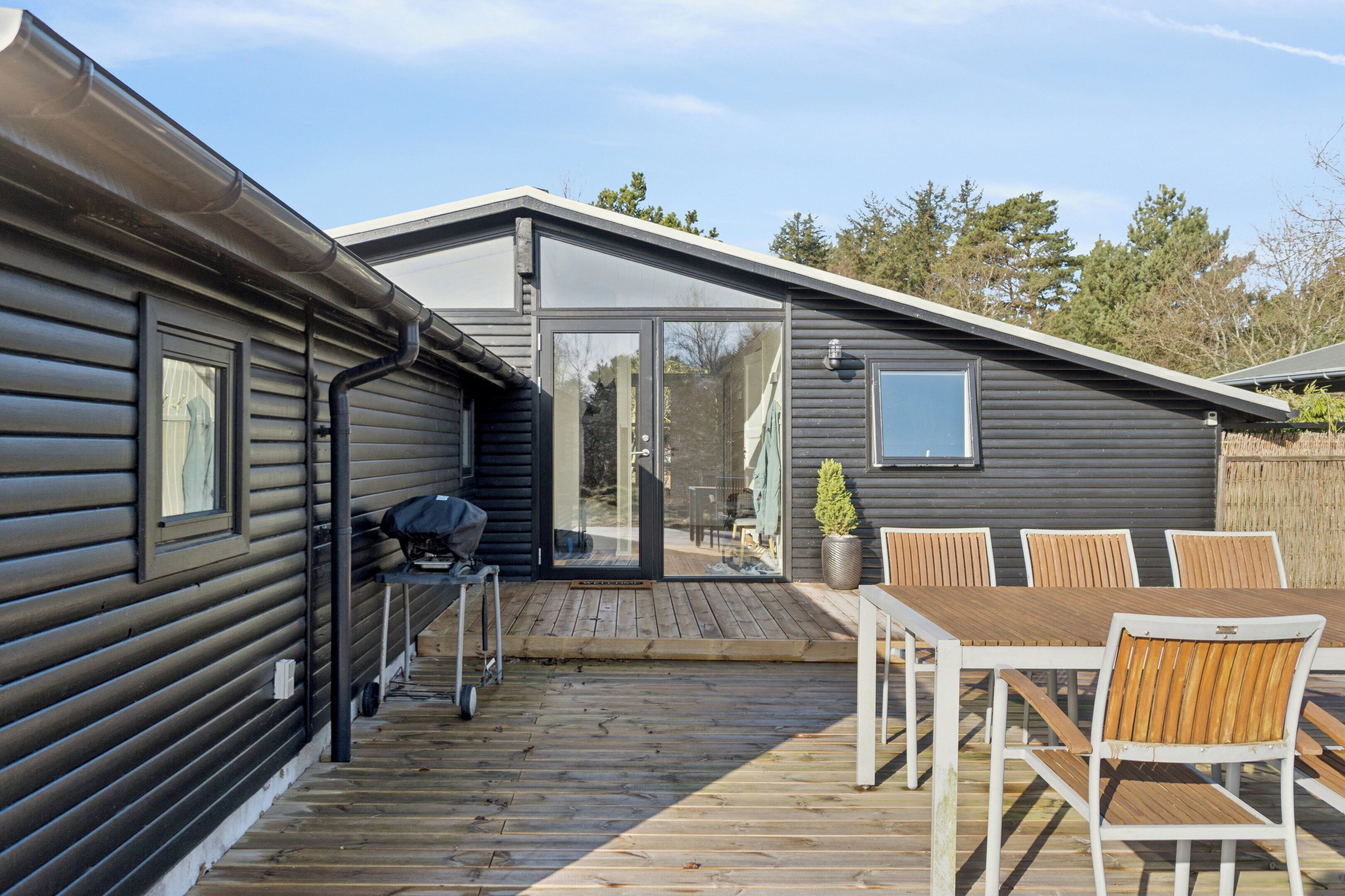 A wooden deck with a table and chairs, a grill, and a sliding glass door leading to a covered patio.