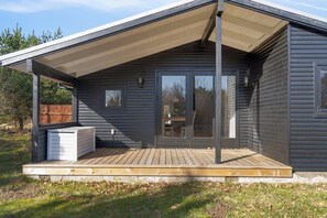 A modern cabin with a wooden deck, a covered porch, and a sliding glass door. - Renovated holiday home near beach and town (Blokhus)