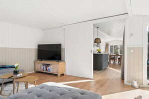A modern living room with a flat-screen TV, a sofa, a coffee table, and a bookshelf. - Renovated holiday home near beach and town (Blokhus)