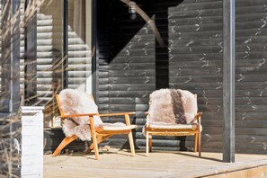 Two wooden chairs with fur upholstery on a wooden deck in front of a log cabin. - Renovated holiday home near beach and town (Blokhus)
