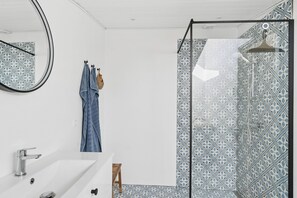 A bathroom with a white sink, a mirror, a towel rack with a blue towel, and a shower with patterned tiles. - Renovated holiday home near beach and town (Blokhus)