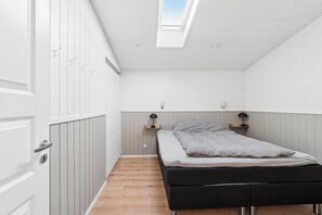 Ein Schlafzimmer mit Dachfenster, einem Bett, einem Kleiderschrank und einem Nachttisch mit Lampe.