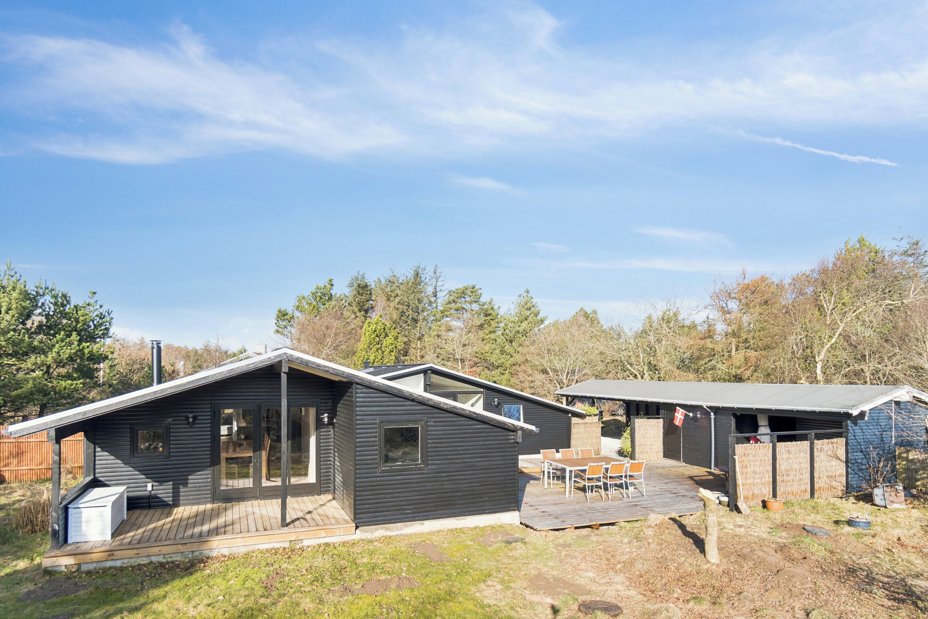 A modern cabin with a deck, a patio area, and a small outdoor seating space.