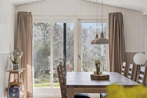 A dining area with a wooden table, chairs, a pendant light, and a view through large windows. - Renovated holiday home near beach and town (Blokhus)