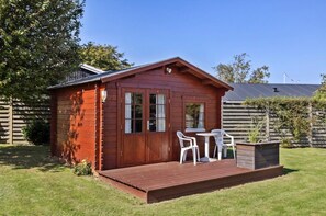 Une cabane en bois avec une terrasse, deux fenêtres et une petite table avec des chaises.