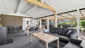 Een moderne woonkamer met een bank, salontafel en stoelen. In de achtergrond is een keuken met een eettafel en stoelen.