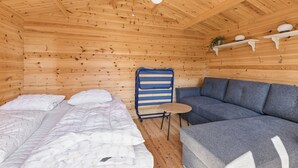 Een houten kamer met een bed, een bank, een tafeltje en planken met decoratieve spullen.