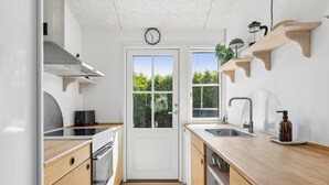 Een moderne keuken met houten kastjes, een ingebouwde oven, een spoelbak en een klok op de deur.