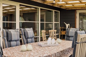 Un espace de restauration en plein air avec une table dressée pour quatre personnes, entourée de chaises rembourrées, sous une pergola en bois.