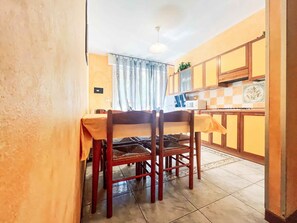 A dining area with a table and chairs, a kitchen in the background, and a ceiling fan. - Holiday apartment with air conditioning and balcony (Bibione)