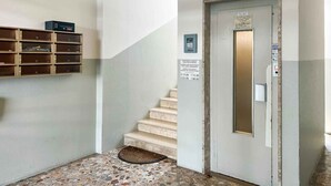 Ein Flur mit Treppe, einer Tür mit Klingelauge, einem Hinweis zu den Ruhezeiten und einem Mülleimer.