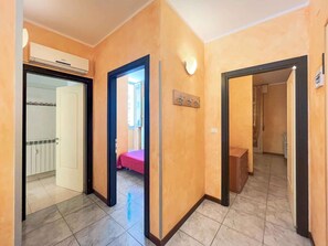A hallway with a tiled floor, a door leading to a room with a bed, and an air conditioning unit on the wall. - Holiday apartment with air conditioning and balcony (Bibione)