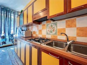 A kitchen with wooden cabinets, a gas stove, and a stainless steel sink. - Holiday apartment with air conditioning and balcony (Bibione)