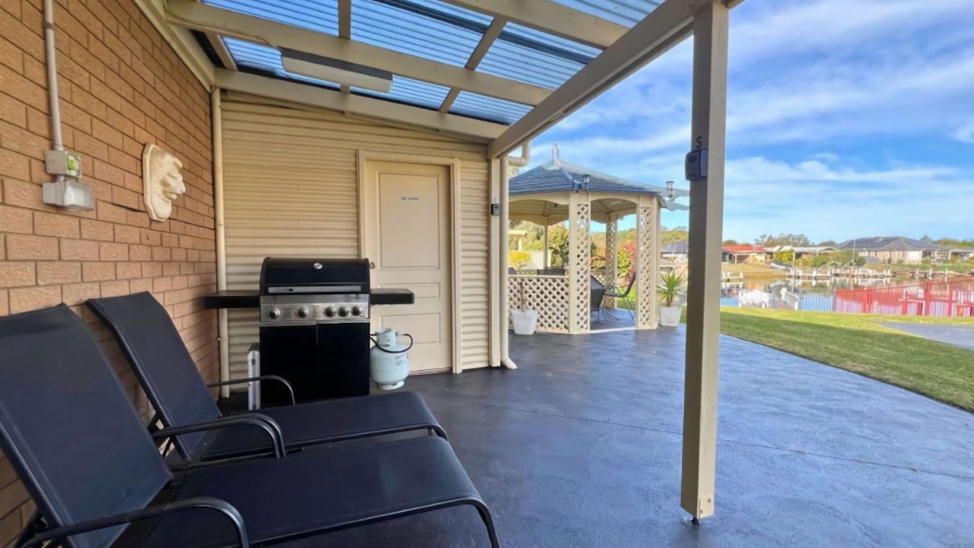 A covered patio with a grill, lounge chairs, and a gazebo in the background.