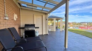 A covered patio with a grill, lounge chairs, and a gazebo in the background.