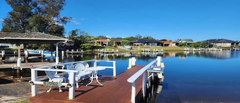 A calm lake with a wooden dock, a gazebo, and a row of houses in the background.