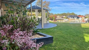 A well-maintained garden with a gazebo, a lawn, and a seating area with chairs. - Chloes Waterfront Oasis ~ A modern apartment with open plan living (Sussex Inlet)
