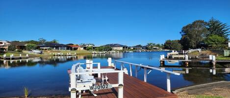 A calm waterfront with a wooden dock, a boat, and a clear blue sky.