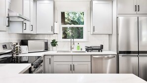 A modern kitchen with stainless steel appliances, white cabinetry, and a window providing natural light. - Newly Modern 4BR2BA Rambler by Super Market (Shoreline)