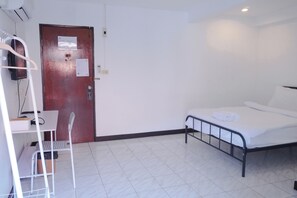 A room with a bed, a desk with a chair, a wardrobe, and a door with a notice on it. - GO INN Patong Beach (Patong)