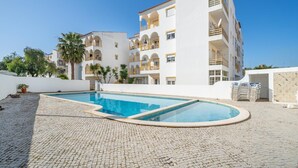 Ett hotell med flera våningar, en swimmingpool, en uteservering och palmer.