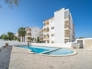 A multi-story hotel with a swimming pool, outdoor seating area, and palm trees. - Comfortable apartment with pool (Lagos)