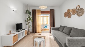 Ett modernt vardagsrum med en grå soffa, en tv på ett vitt tv-bord, ett litet vitt bord och en växt.