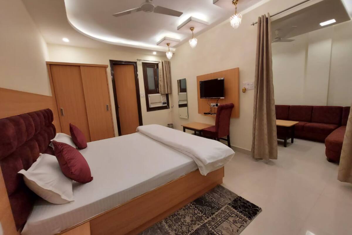 A modern hotel room with a large bed, a desk, a sofa, and a TV.