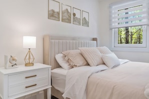 Et soveværelse med seng, natbord, lampe og billedkunst på væggen.