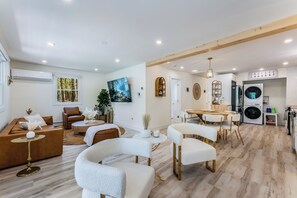 A modern living room with a brown leather sofa, white armchairs, and a dining area with a wooden table and chairs. - White Cabin by Lake w/Hot Tub Sauna & Game Room (ALBRIGHTSVLLE)