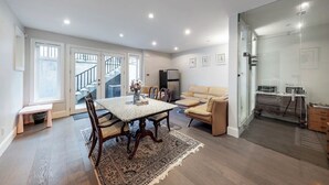Een ruime woonkamer met een eettafel, een bank en een keuken met een koelkast en magnetron.