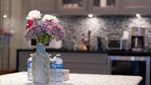 Een marmeren vaas met bloemen op een tafel, waterflessen en een keuken op de achtergrond.