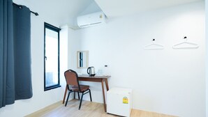 Ein kleiner, sauberer Raum mit Schreibtisch aus Holz, einem Stuhl, einem kleinen Kühlschrank und einem Fenster mit Vorhängen.