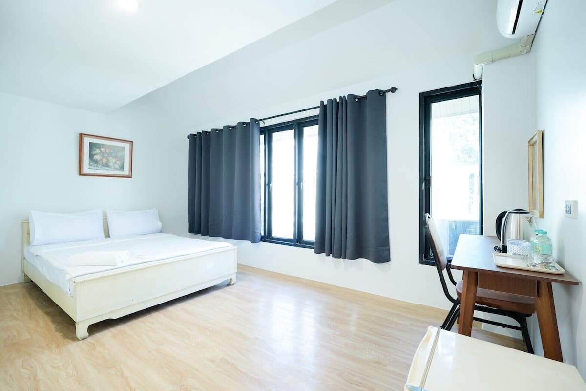 Ein Zimmer mit einem Bett, einem Schreibtisch mit Stuhl und zwei Fenstern mit Vorhängen.