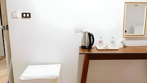 Ein kleines Zimmer mit einem Holztisch, einem Wasserkocher, einem Spiegel und einigen Pflegeartikeln.