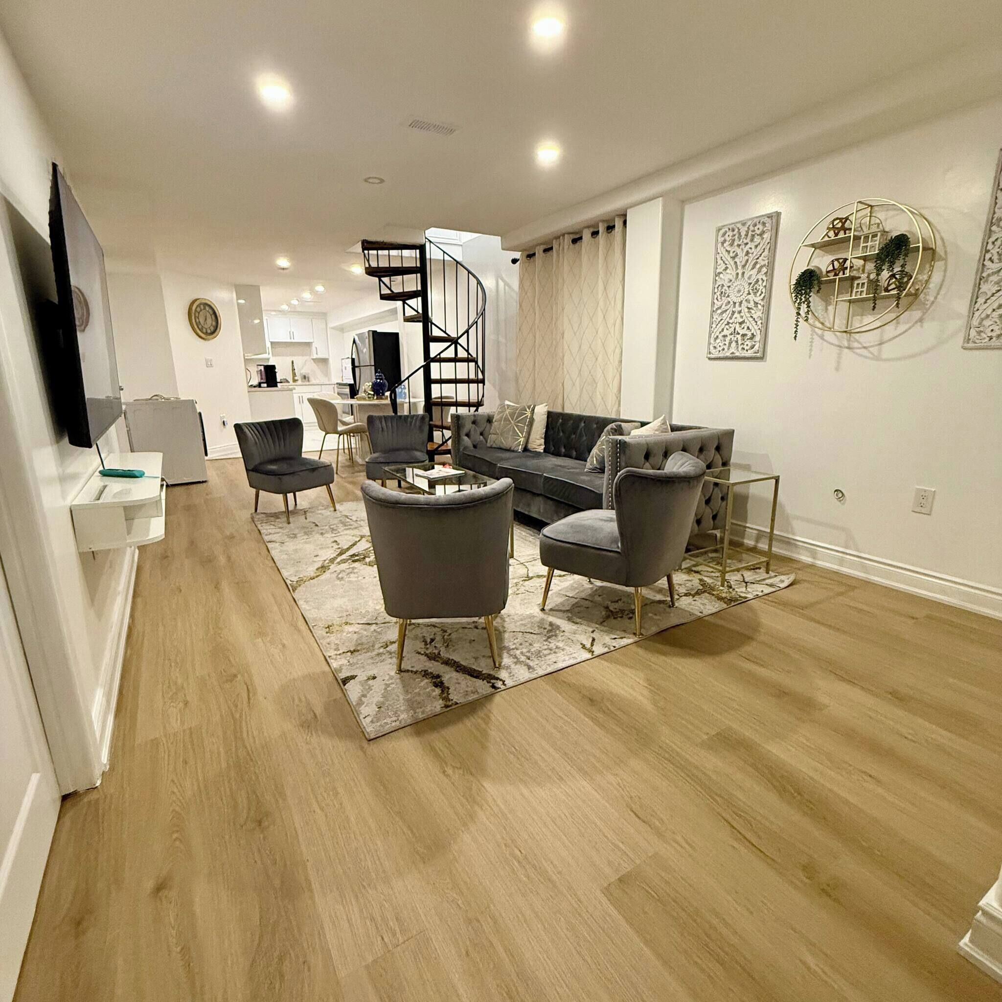 A modern living room with a sofa, armchairs, and a coffee table. There is a spiral staircase leading to an upper level.